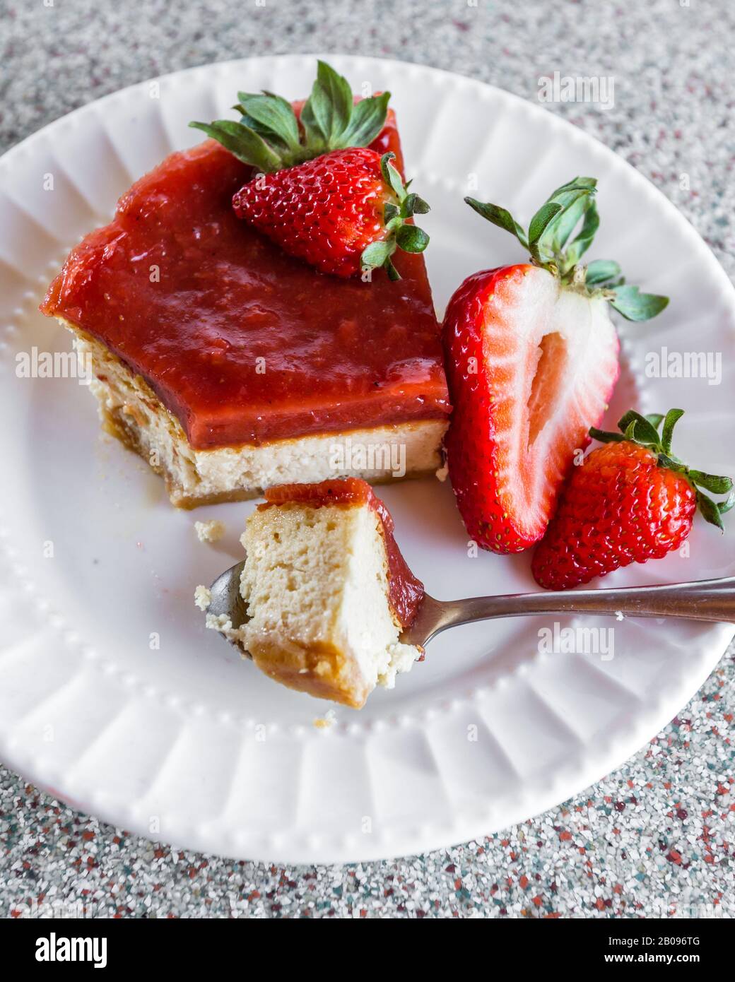 rebanada de tarta de queso con una capa de mermelada de fresa encima servida en un plato blanco con bayas frescas como guarnición Foto de stock