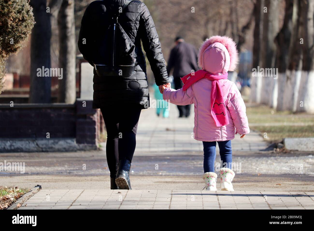 Mamá y su hija están caminando por la calle de invierno con las manos. Mujer joven y esbelta llevar niña pequeña, concepto de maternidad, madre soltera Foto de stock