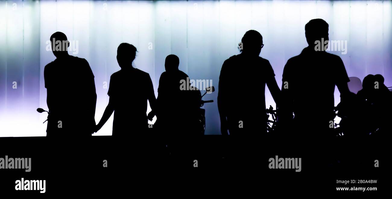 Siluetas de la gente caminando por la noche, frente al edificio moderno, en alto contraste blanco negro y púrpura Foto de stock