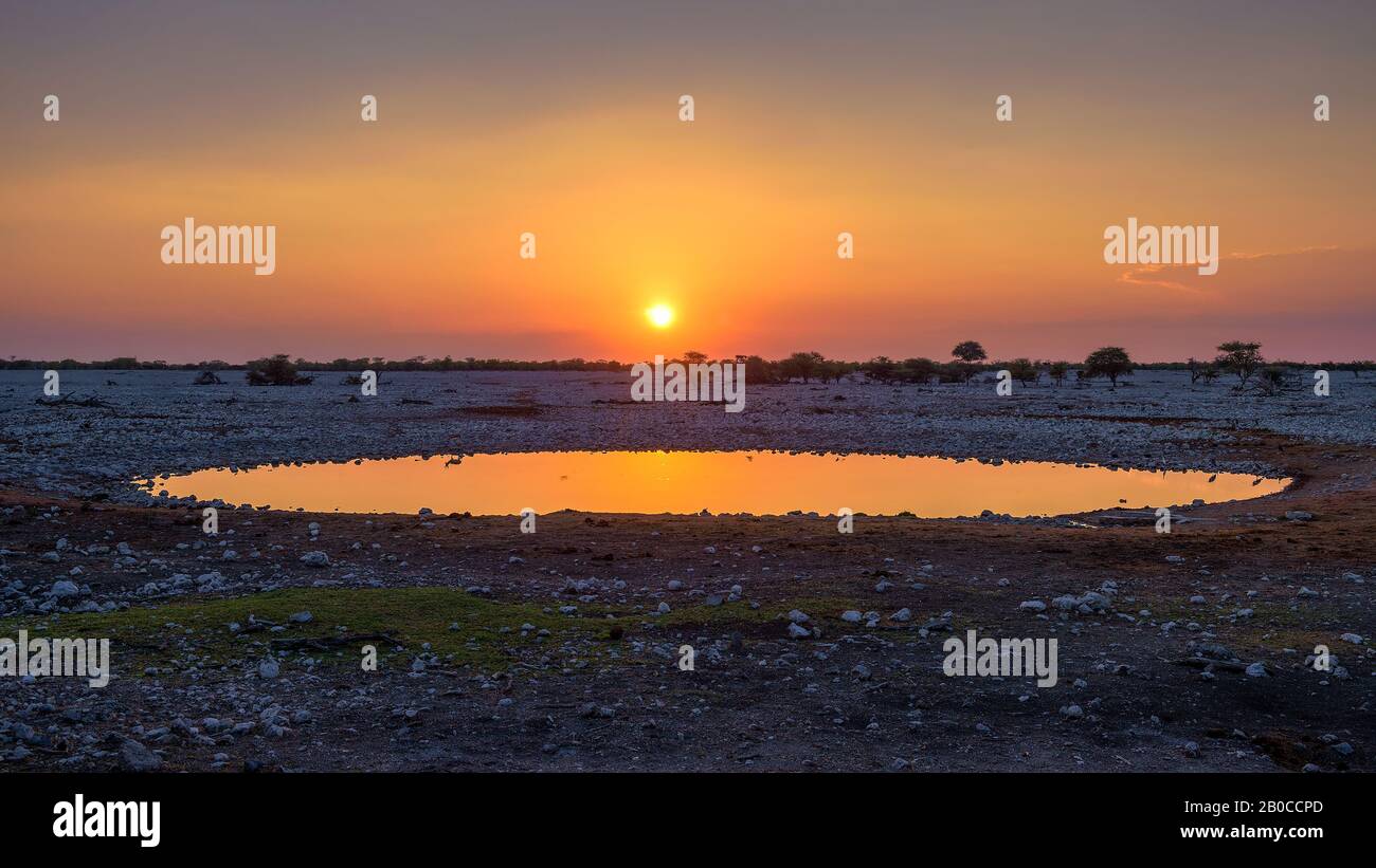 Puesta de sol sobre el agujero de agua del campamento de Okaukuejo en Etosha, Namibia Foto de stock