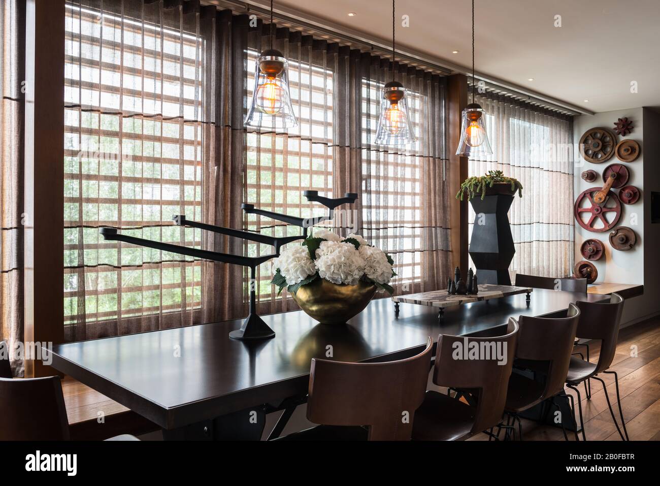 Lámparas colgantes de vidrio sobre mesa de comedor con hidrangea en jarrón de cobre Foto de stock
