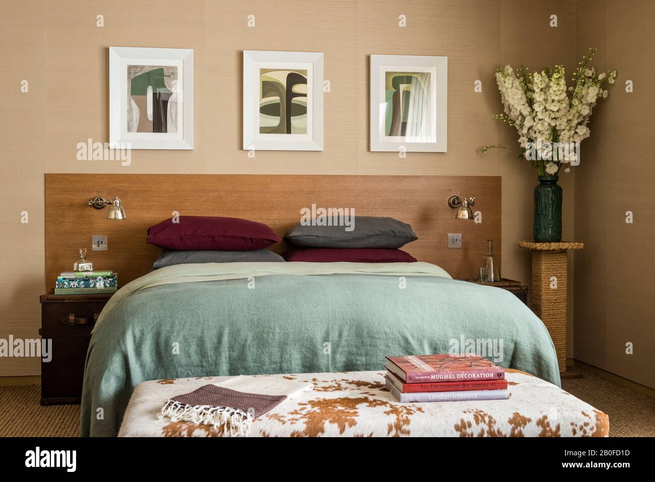 Arte moderno sobre la cama doble con manta verde claro y libros sobre el taburete de la footfootfool de cowhide. Foto de stock
