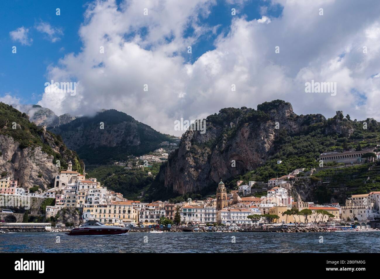 El colorido pueblo de Amalfi visto desde el mar, con espectaculares montañas y cielos de verano en el fondo, en la costa de Italia Foto de stock
