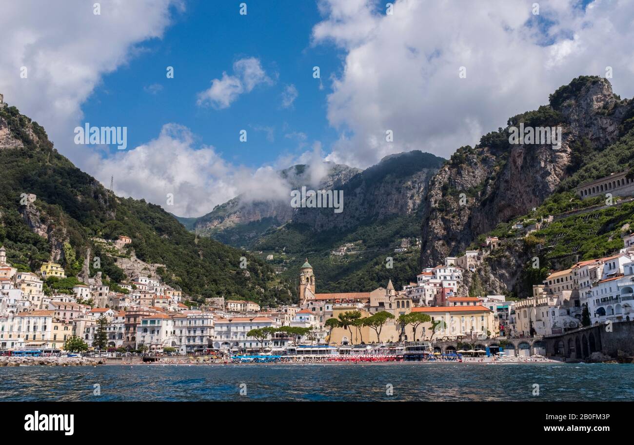 El colorido pueblo de Amalfi visto desde el mar, con espectaculares montañas y cielos de verano en el fondo, en la costa de Italia Foto de stock
