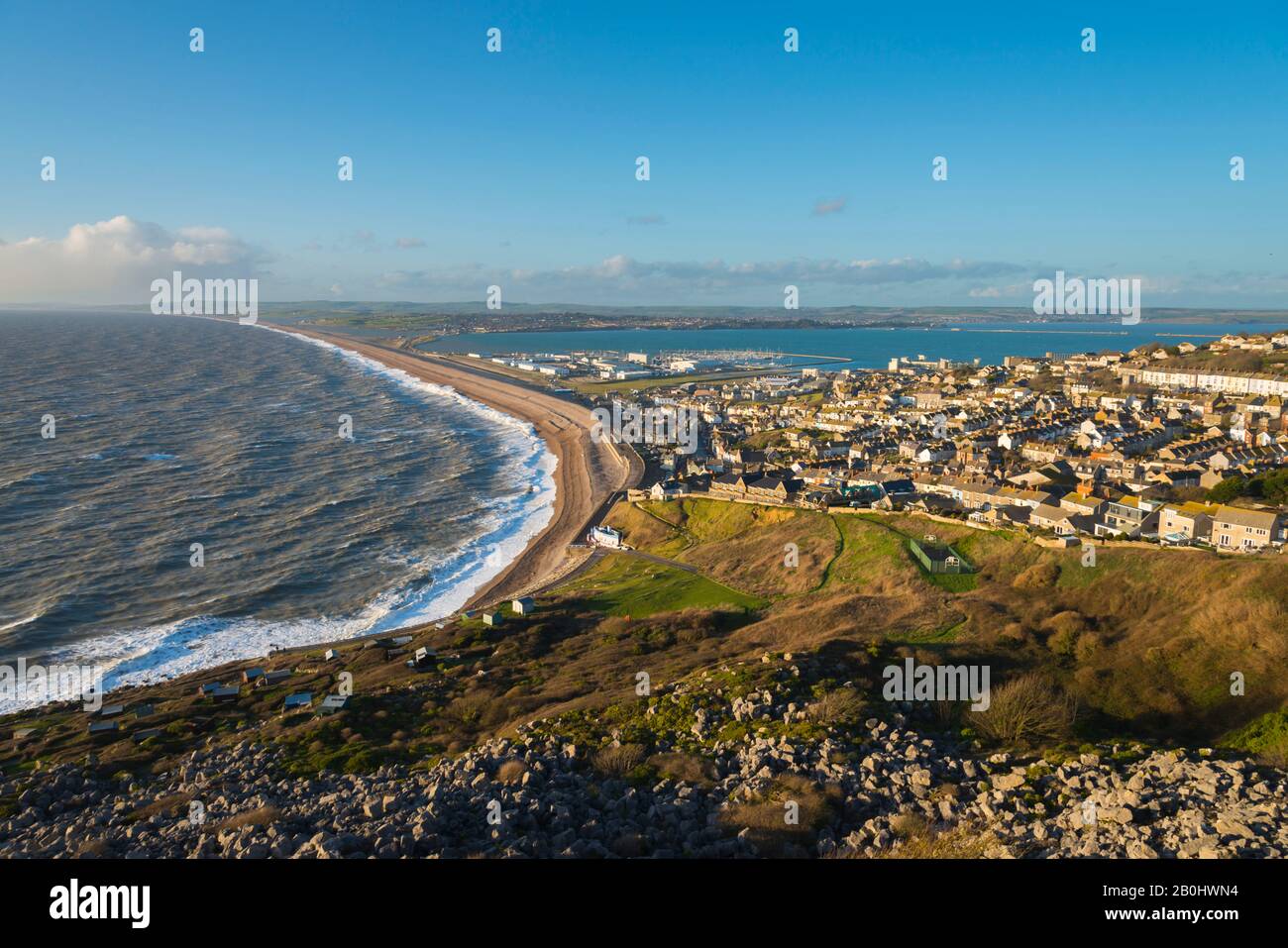 Fortuneswell, Portland, Dorset, Reino Unido. 20 de febrero de 2020. El tiempo en Reino Unido. Vista desde la cima de los acantilados de West Weares a través de Fortuneswell en la isla de Portland en Dorset durante el sol de última hora de la tarde con vientos y mares agitados rompiendo en tierra en Chesil Beach en Chiswell. Crédito De La Imagen: Graham Hunt/Alamy Live News Foto de stock