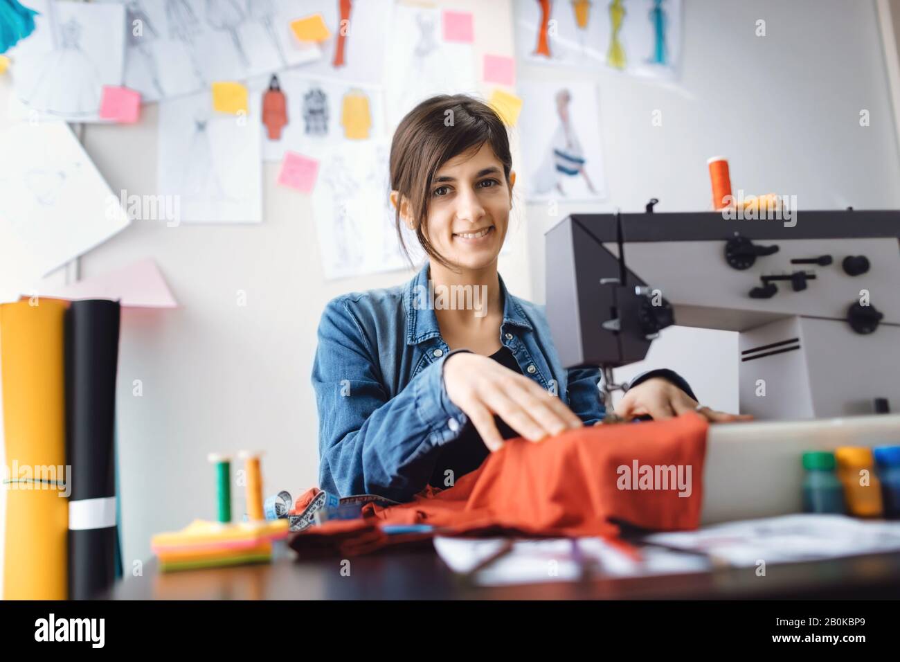 Joven diseñador de costura en el taller. Trabajo a medida en máquina de coser. Concepto de pequeña empresa. Foto de stock