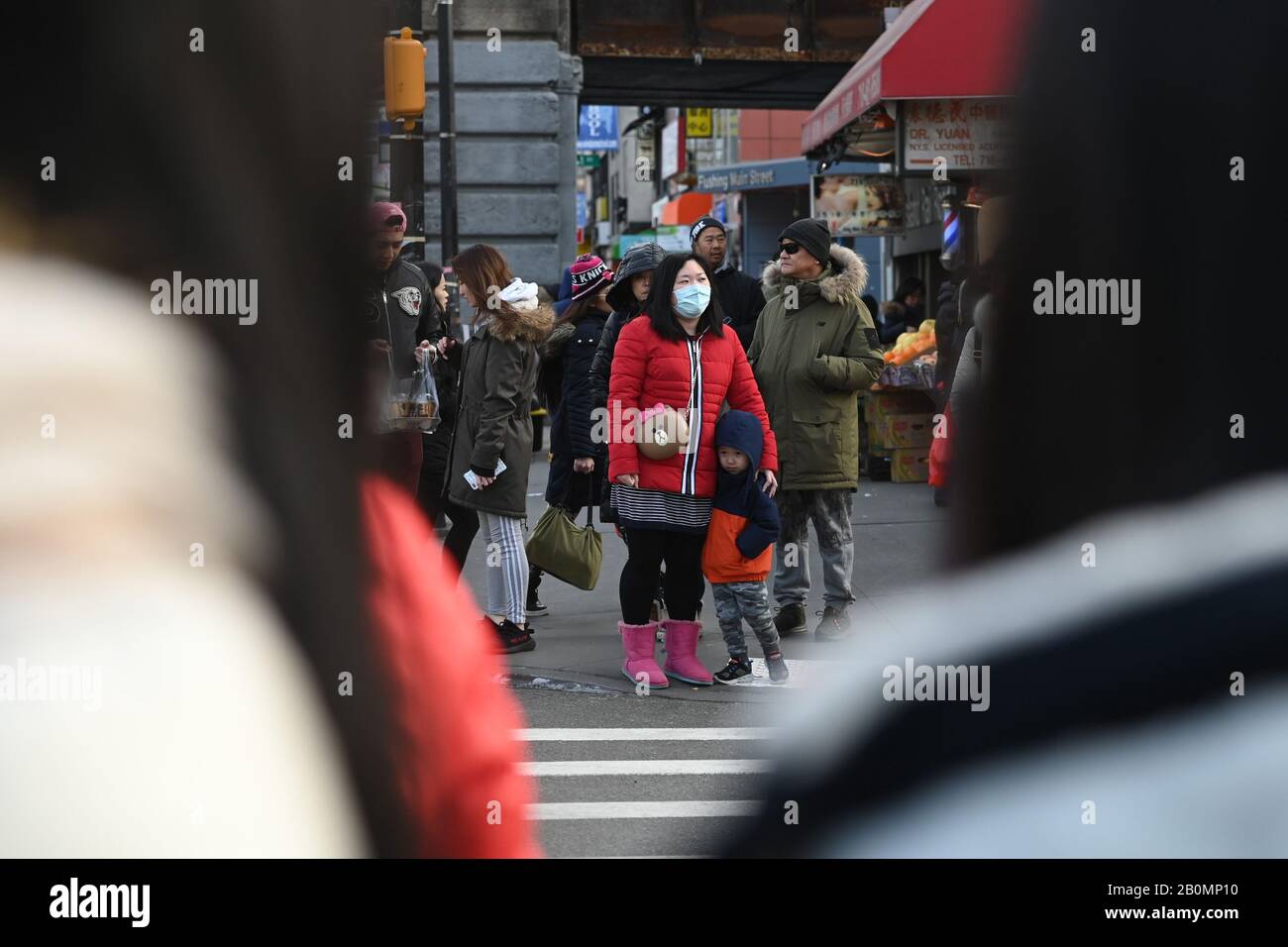 Nueva York, EE.UU. 20 de febrero de 2020. Una mujer usa una máscara protectora mientras espera con su hijo para cruzar la calle en la sección de Flushing del distrito de Queens, NY, en la ciudad de Nueva York, el 20 de febrero de 2020. La Organización Mundial de la Salud ha declarado una emergencia mundial de salud pública a medida que los casos de las nuevas infecciones mortales por coronavirus COVID-19 ascienden a más de 75,000 en todo el mundo y las muertes reportadas superan los 2000. (Anthony Behar/Sipa Usa) Crédito: Sipa Usa/Alamy Live News Foto de stock