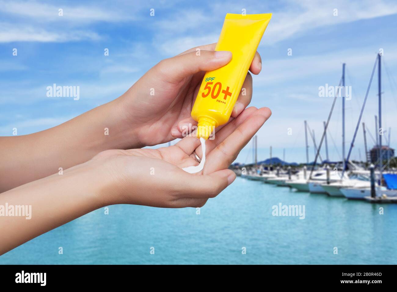 mujer aplicando protector solar en su mano con botes borrosos atracados en el fondo del club náutico. Concepto de protección solar SPF. Vacaciones de viaje Foto de stock