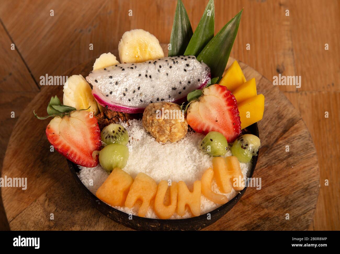 Ensalada de frutas orgánicas en cuenco con granola, sin azúcar y Ferrero Rawcher en tabla de madera. Alimentos saludables. Foto de stock