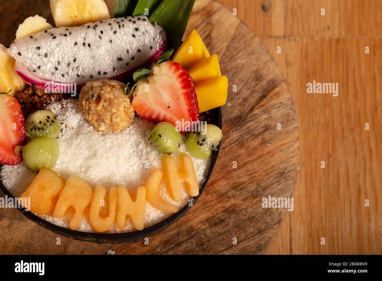 Primer plano tomado de arriba de ensalada de frutas orgánicas en un tazón con granola, sin azúcar y Ferrero Rawcher en una tabla de madera. Alimentos saludables. Isolat Foto de stock