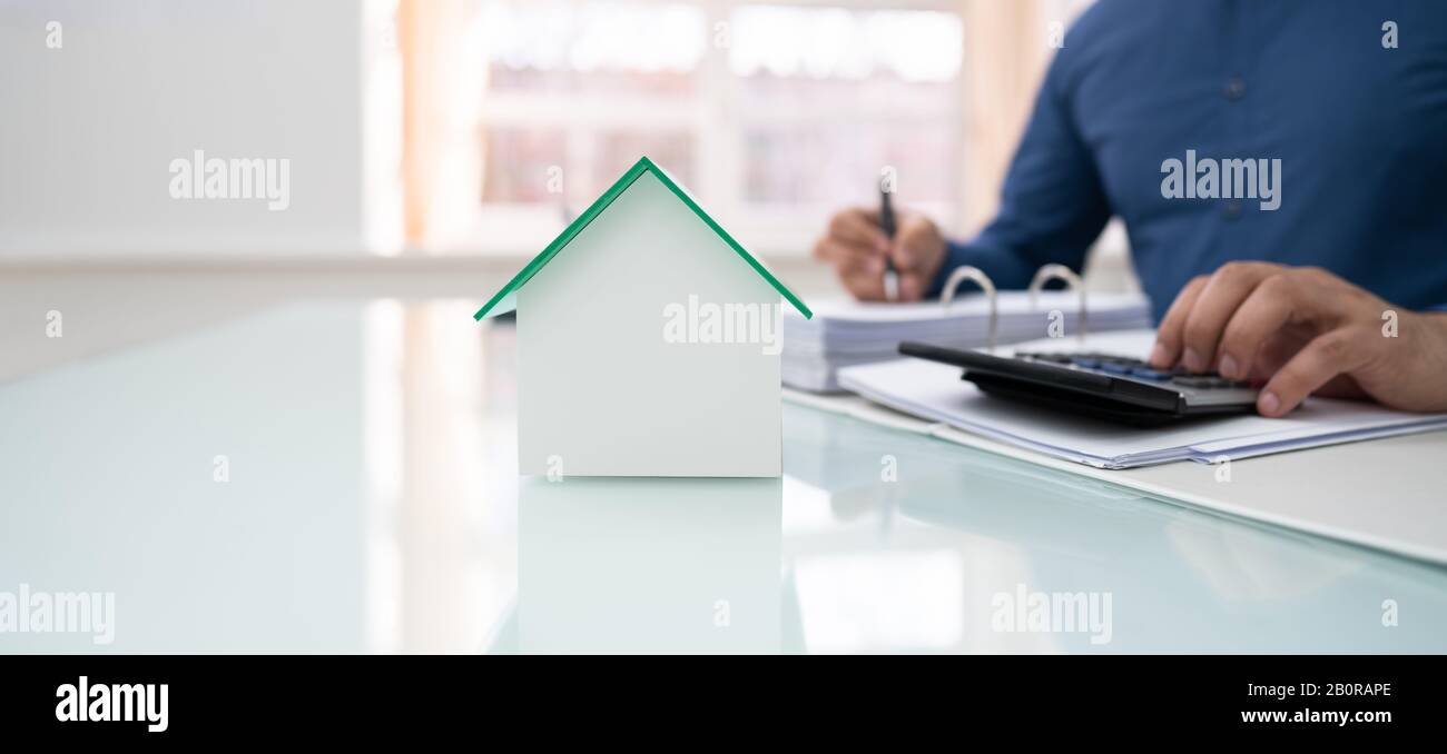 Sección Intermedia De Businessman Calculating Invoice With House Model En Office Foto de stock