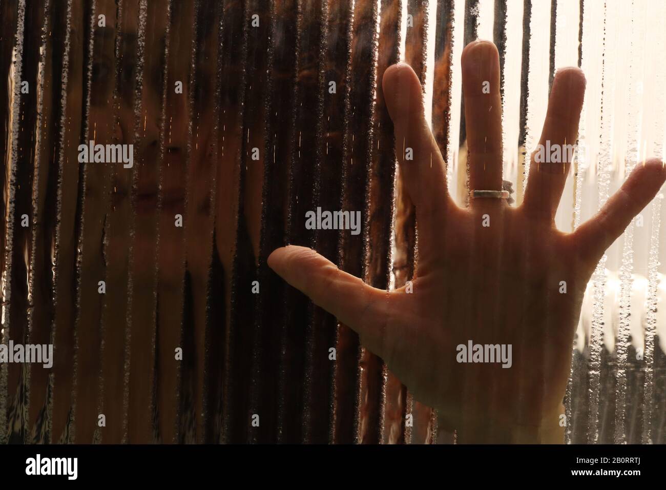 Imagen espeluznante de la niña detrás del cristal con las palmas de las manos sobre el cristal texturizado Foto de stock