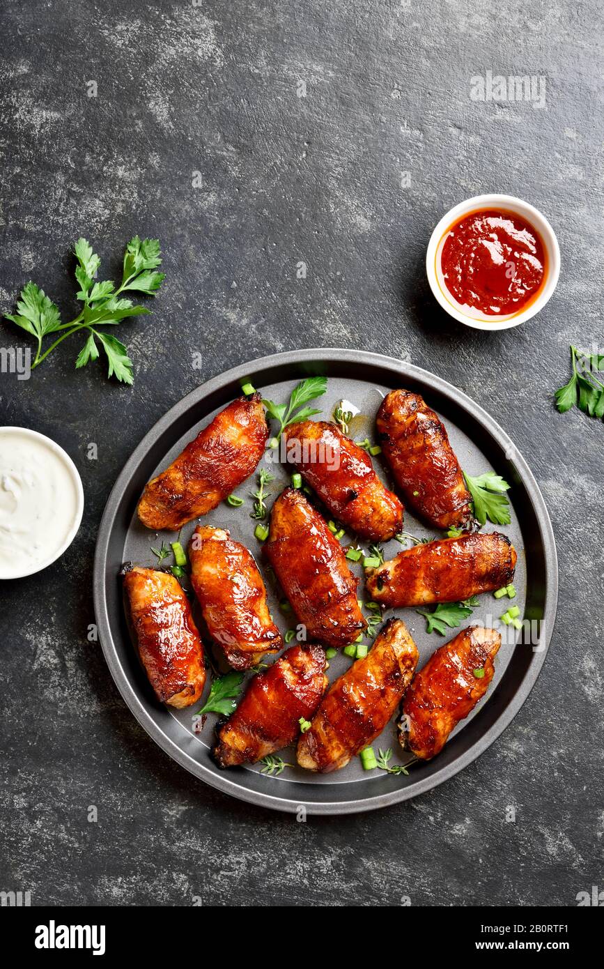 Sabrosas alas de pollo a la parrilla envueltas con bacon sobre fondo de piedra oscura y espacio libre. Sabroso aperitivo de carne de pollo, tocino en dulce, agrio, sa Foto de stock