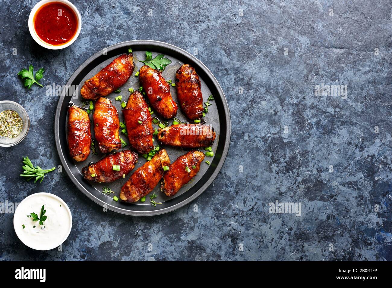 Panceta envuelta alas de pollo a la parrilla sobre fondo de piedra azul con espacio libre. Sabroso aperitivo de carne de pollo, tocino en dulce, agrio, salado an Foto de stock