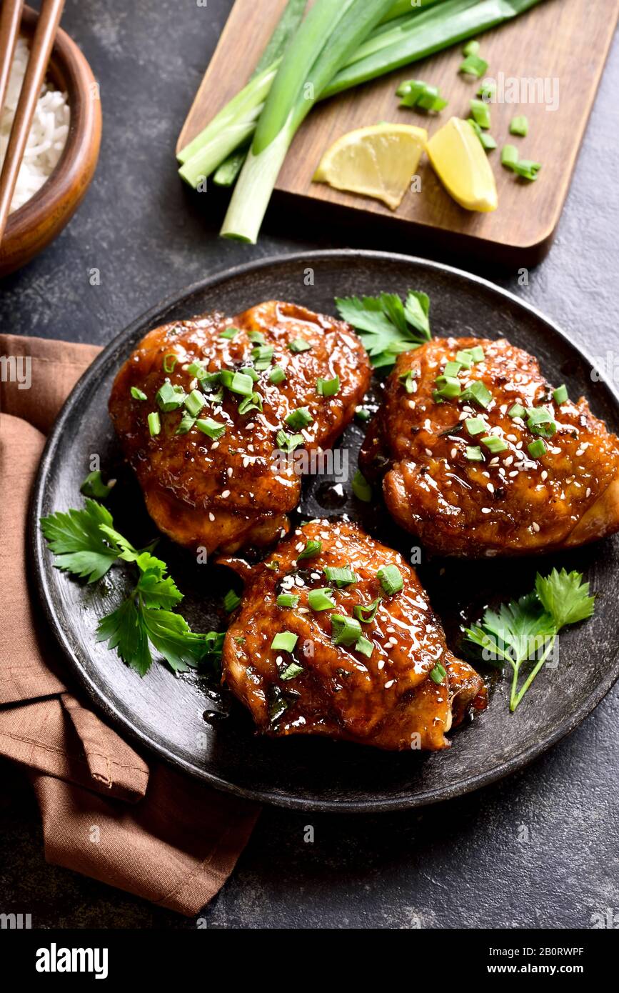 Dulce y picante miel muslos de pollo a la parrilla en la placa sobre fondo de piedra oscura. Comida sabrosa en un estilo asiático. Foto de stock