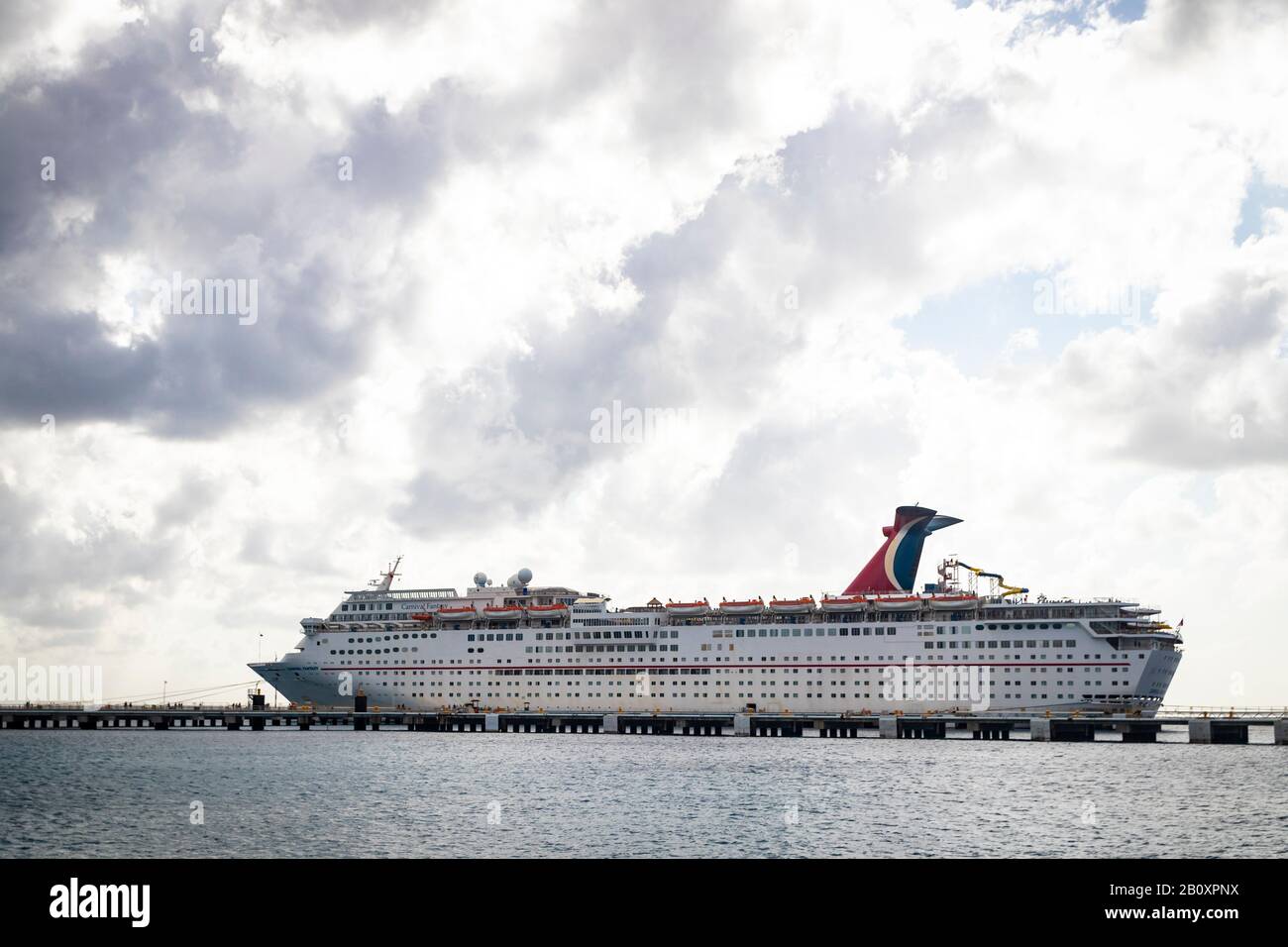 Vista lejana del crucero 'Carnaval Fantasy', en el puerto de Cozumel bajo el cielo nublado Foto de stock