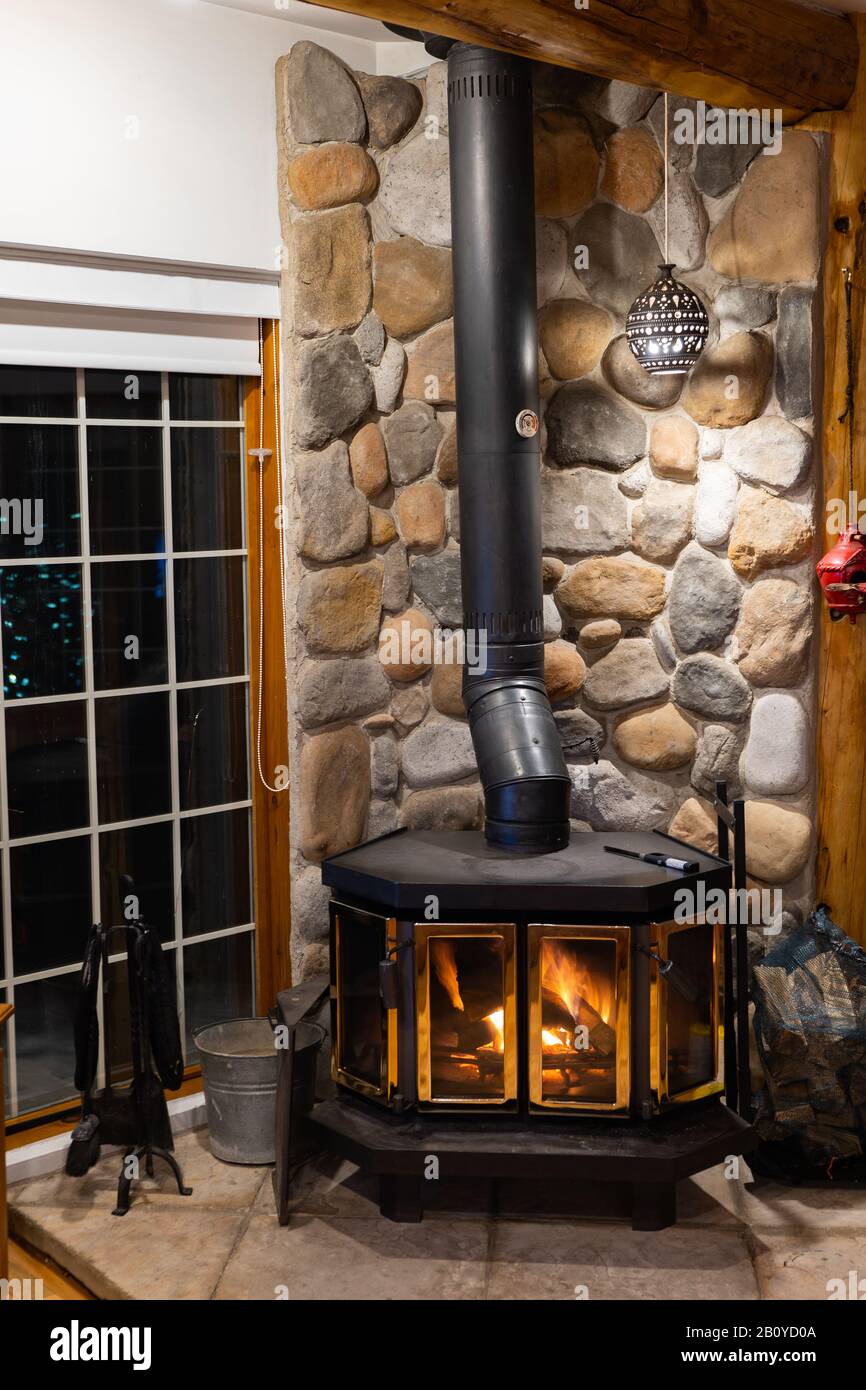 Chimenea de leña con cuerpo de metal y puerta de vidrio en la casa con un interior acogedor. Foto de stock