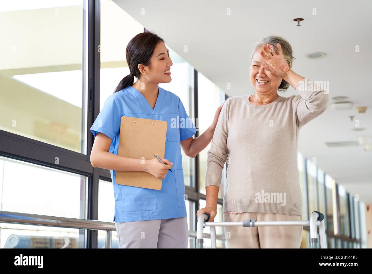 mujer asiática mayor que se limpia del sudor de la frente durante la sesión de fisioterapia en el centro de rehabilitación Foto de stock
