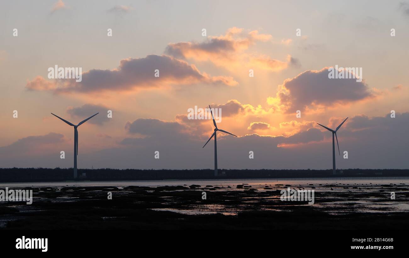 Turbinas eólicas en la zona costera, con puesta de sol y un cielo nublado por la noche. Foto de stock