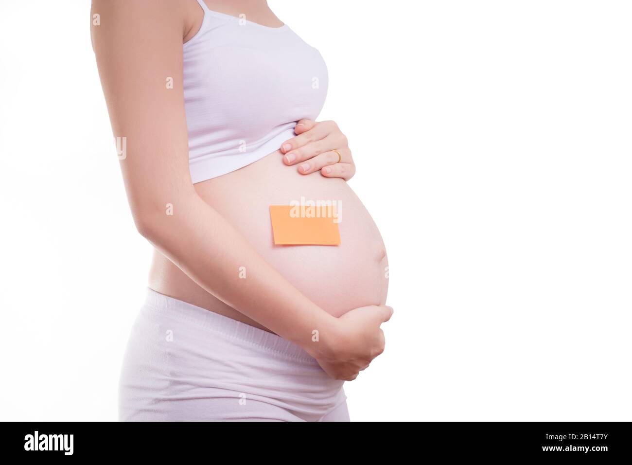 Mujer embarazada con un bloc de notas en blanco en su vientre, cara anónima. Hermosa Asia modelo femenino en sus 20. Mujer embarazada aislada en negro blanco Foto de stock