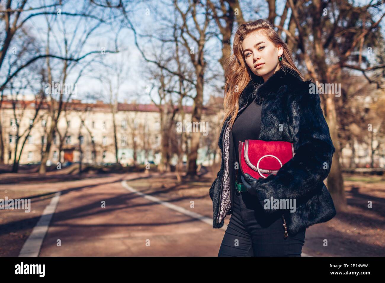 Mujer joven con estilo con abrigo de piel y cartera roja en el parque. Moda  femenina. Accesorios para ropa de moda de primavera Fotografía de stock -  Alamy