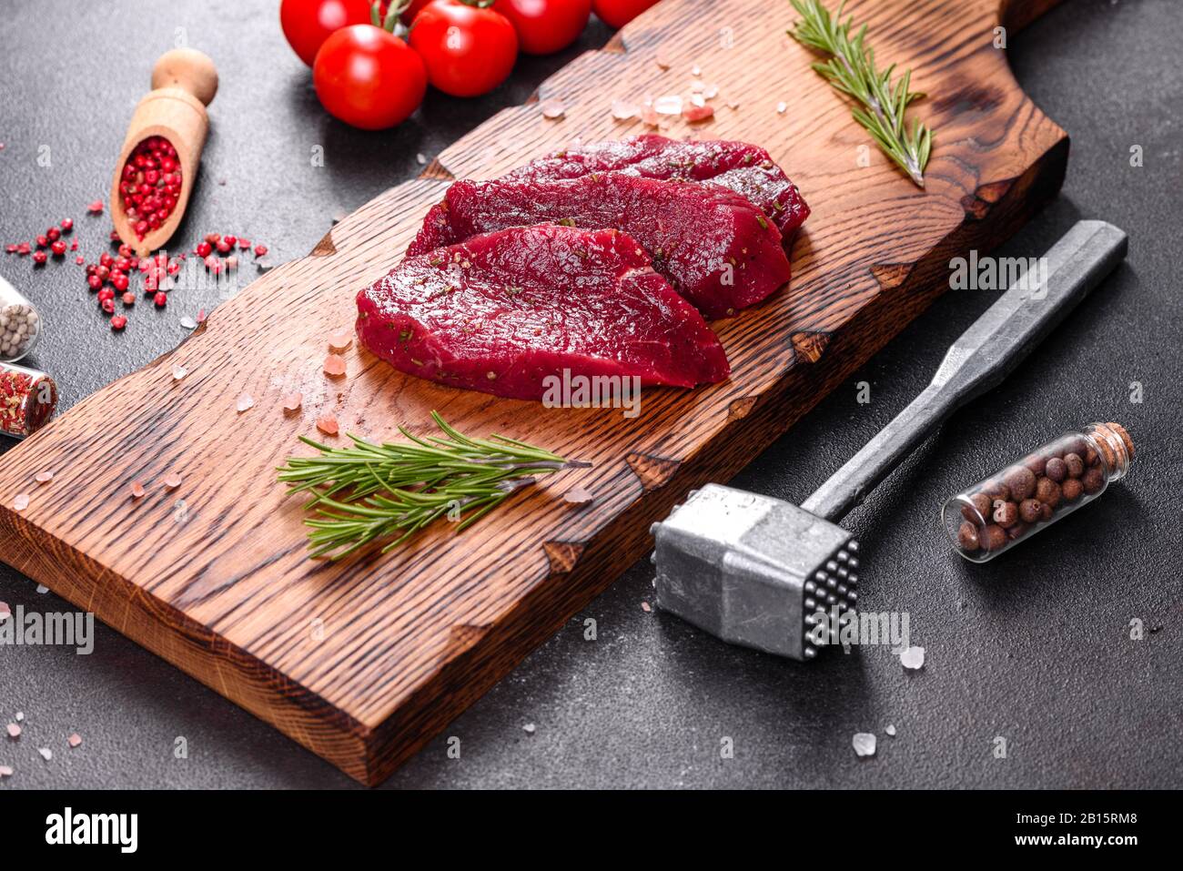 Filete de ternera fresca Mignon, con sal, pimienta, tomillo, tomates. Carne de mármol fresca cruda carne de bistec y condimentos sobre un fondo oscuro Foto de stock