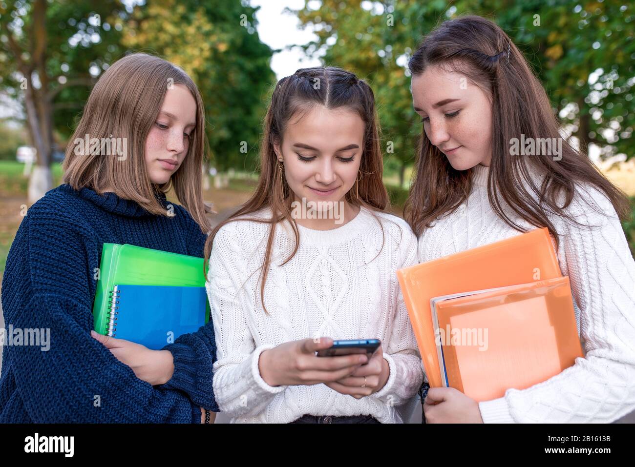 Tres niñas, colegialas, adolescentes de 12-15 años de edad, parque de  verano, ver videos por teléfono, carpetas portátiles resúmenes con libros  de texto. Descanso escuela Fotografía de stock - Alamy