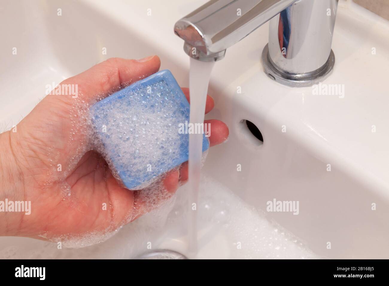 Sosteniendo una barra azul de jabón bajo el grifo en un lavabo del cuarto de baño. Concepto de limpieza médica Foto de stock