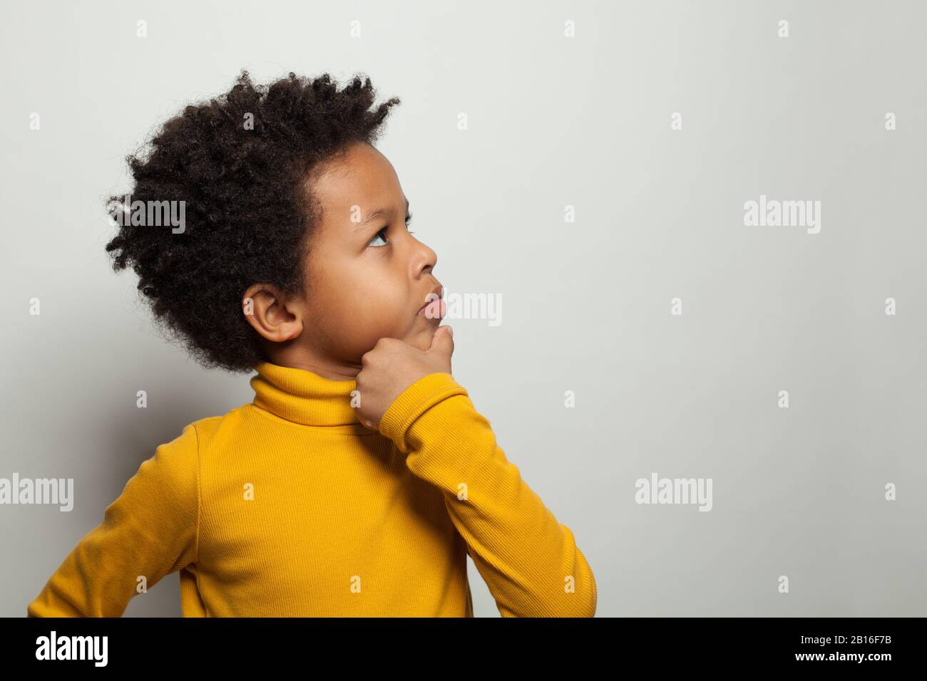 Niño pequeño negro pensando y mirando hacia arriba sobre fondo blanco Foto de stock