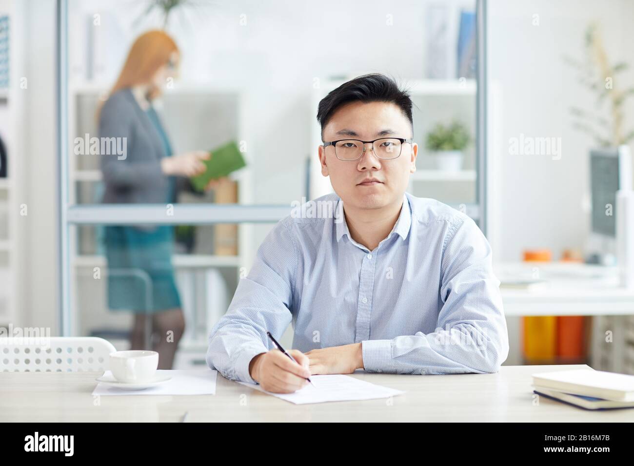 Retrato de un joven hombre de negocios asiático con gafas y mirando la cámara mientras se posaba en el lugar de trabajo en el armario de la oficina, espacio para copias Foto de stock