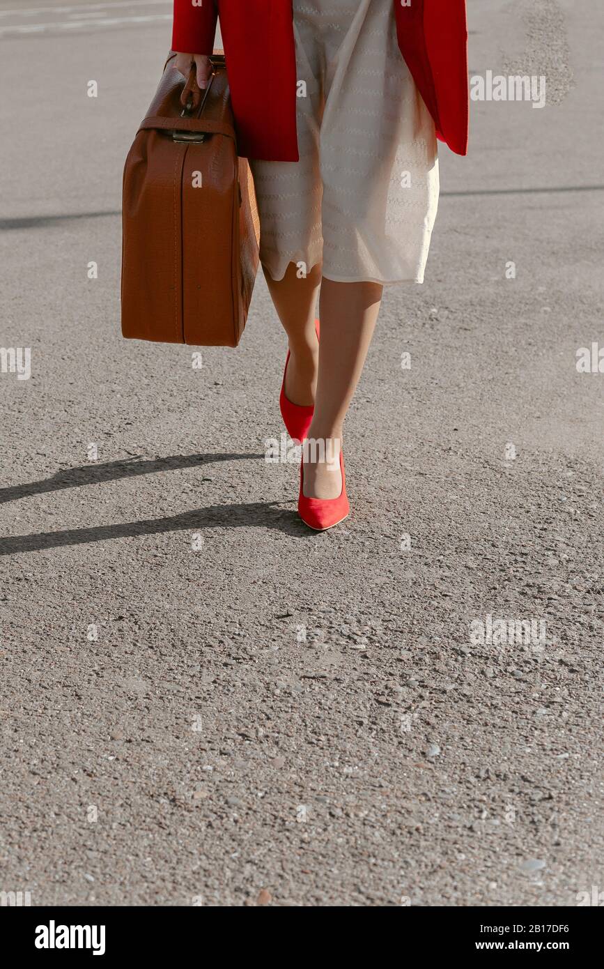 Mujer turística viajero con zapatos rojos y un abrigo va con una maleta.  Las mujeres que viajan al extranjero viajan los fines de semana para una  escapada Fotografía de stock - Alamy