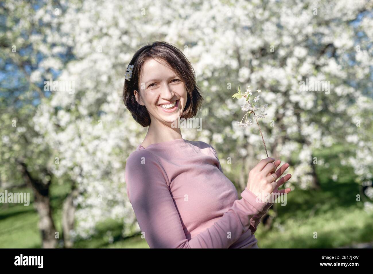 Retrato de una mujer feliz con ramita de cerezo en flor en el jardín Foto de stock