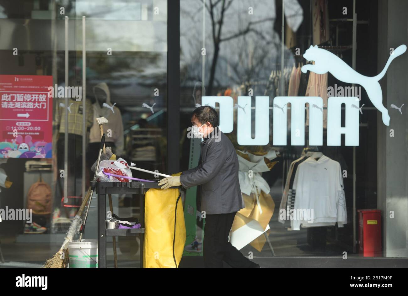Un trabajador de limpieza chino que usa una máscara facial para prevenir el  nuevo coronavirus y la neumonía empuja su carro a pasar por una tienda de ropa  deportiva de Puma en
