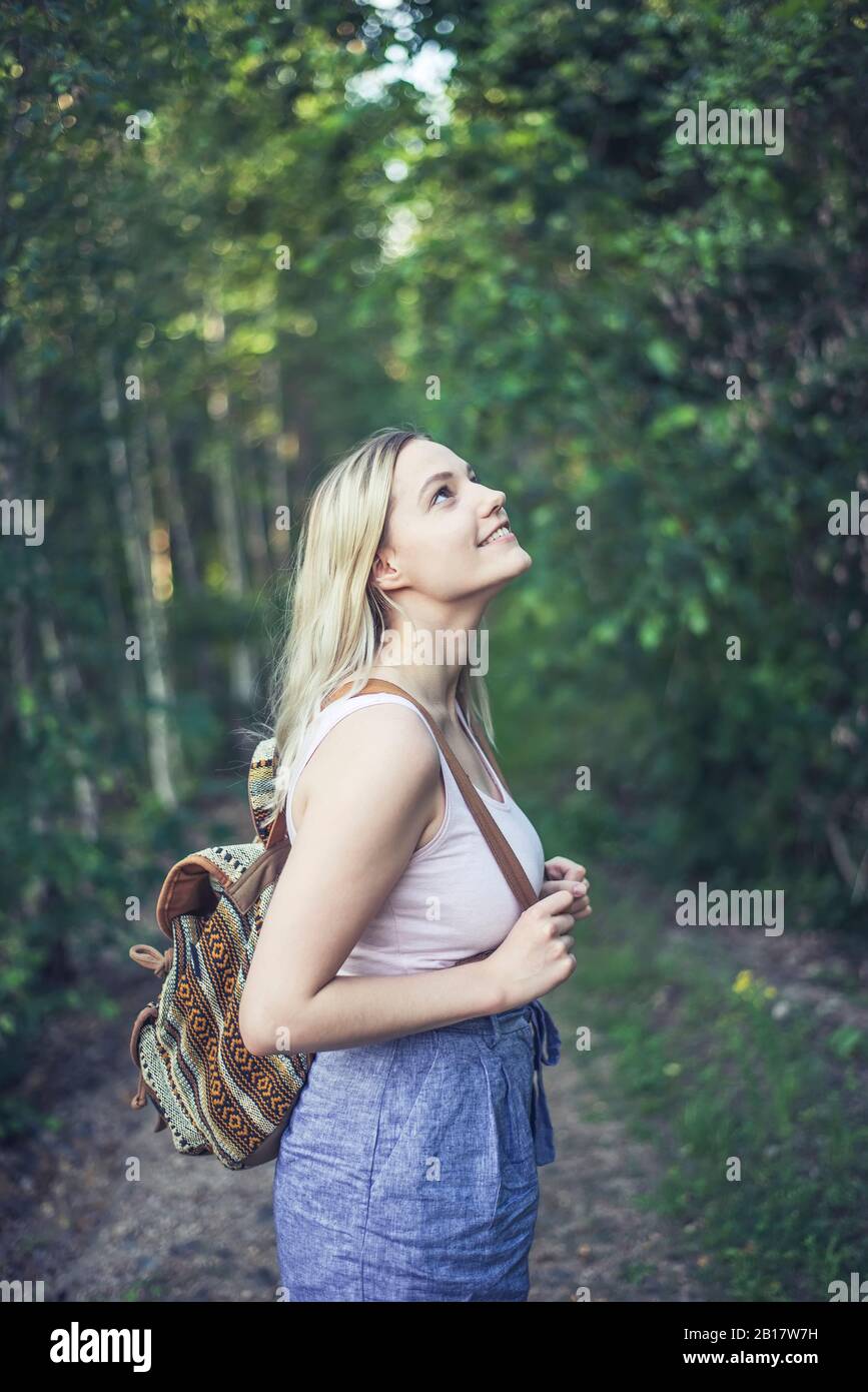 Mujer joven sonriente con mochila en el bosque viendo algo Foto de stock