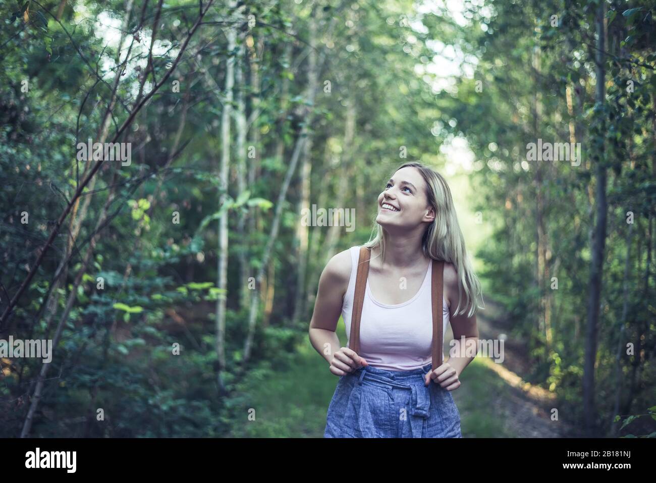 Retrato de una joven sonriente con mochila en el bosque viendo algo Foto de stock