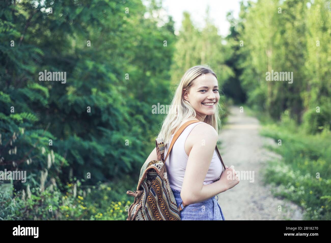 Retrato de una joven sonriente con mochila en la pista del bosque Foto de stock