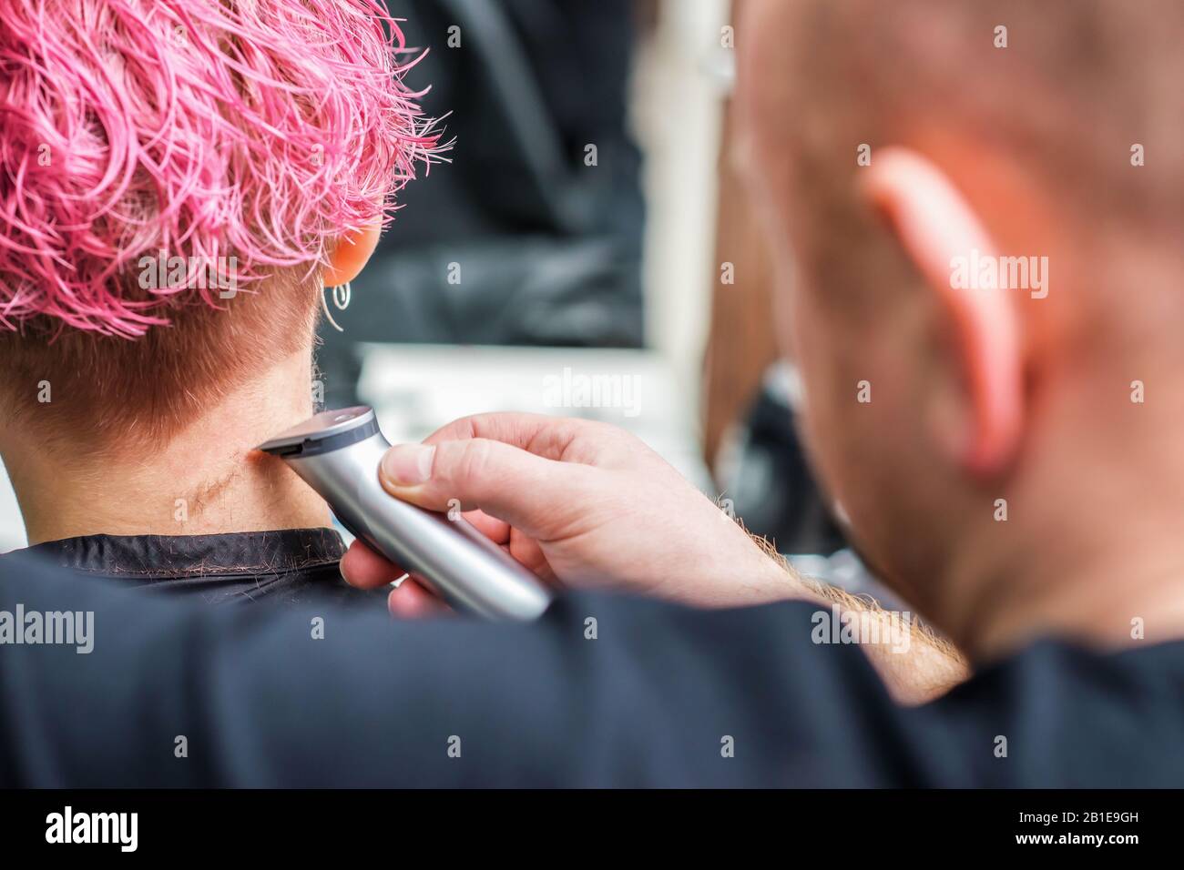 El primer plano de peluquería afeita el cabello de la mujer con afeitadora eléctrica en el salón de belleza. Foto de stock