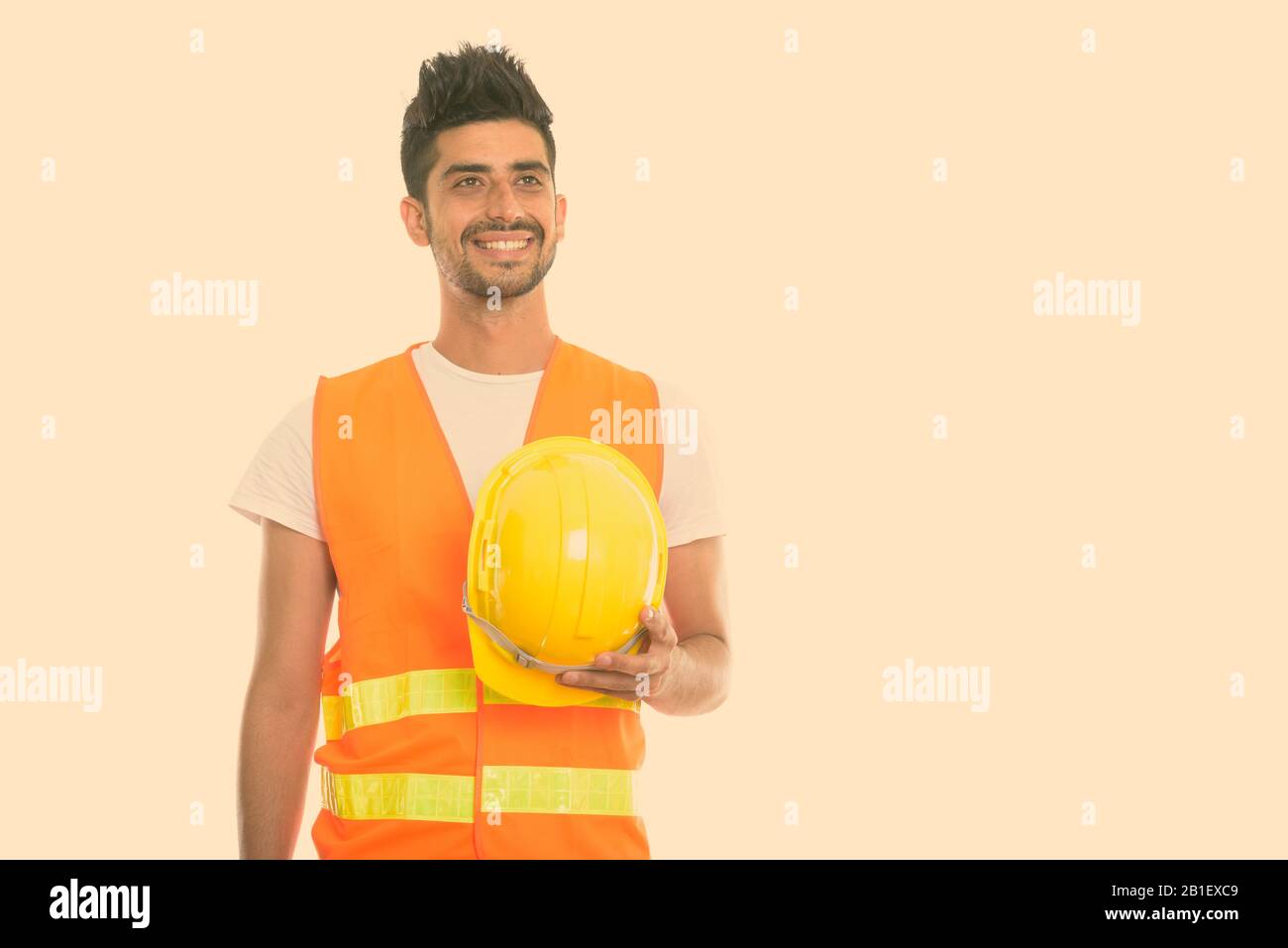 Pensativo feliz el hombre persa, trabajador de la construcción sonriendo mientras mantiene sombrero duro Foto de stock