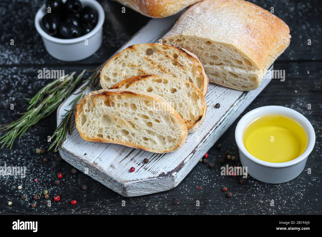 Ciabatta con romero, aceite de oliva y tomates cherry sobre una tabla de madera. Sobre un fondo oscuro. Espacio de copia Foto de stock