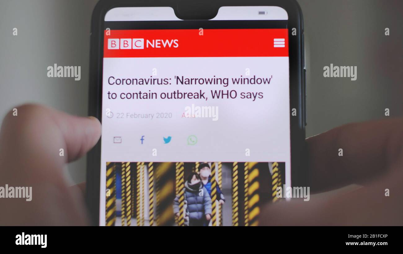 Manos en el smartphone lea el artículo de noticias de Coronavirus covid-19 de la BBC Foto de stock