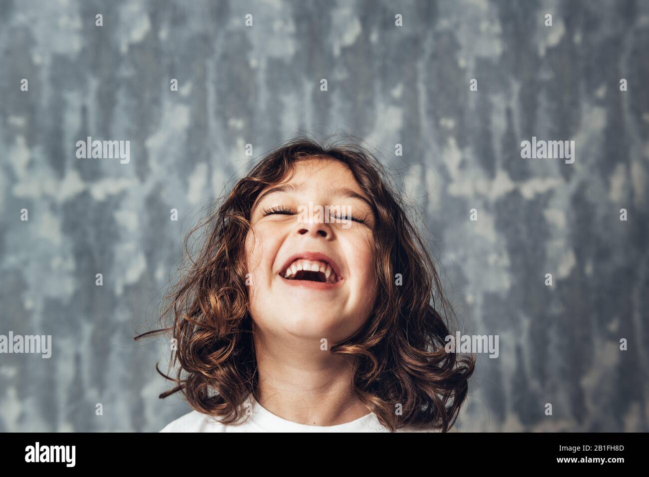 retrato de una niña feliz riendo sobre un fondo azul, feliz infancia y concepto de estilo de vida, copiar espacio para el texto Foto de stock