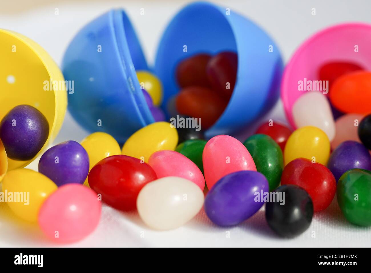 Los coloridos granos de gelatina se derraman de los huevos de Pascua de plástico Foto de stock
