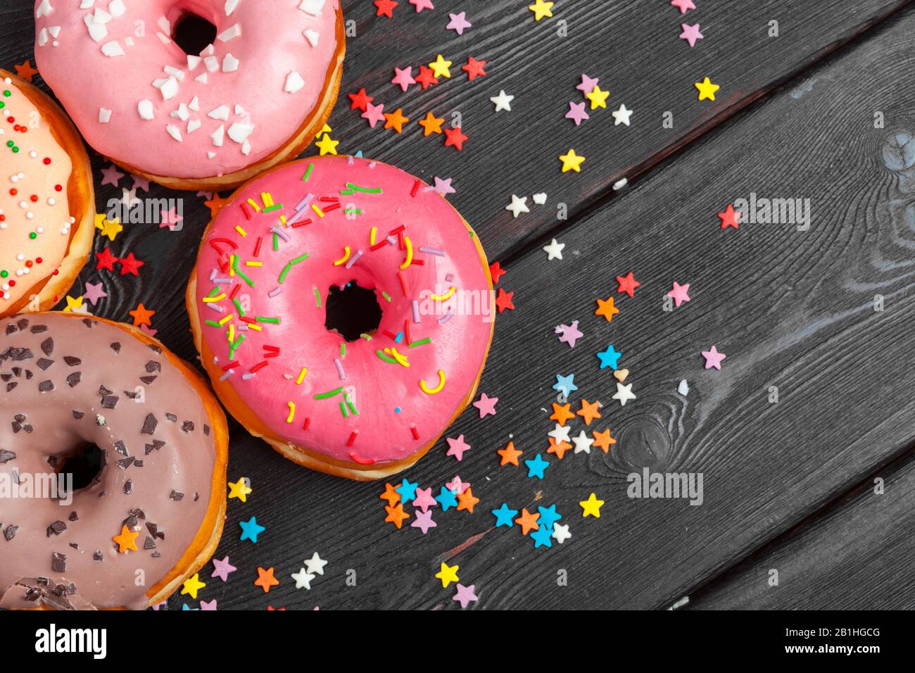 Surtido de rosquillas coloridas decoradas con confeti de colores salpicados  sobre fondo de madera oscura Fotografía de stock - Alamy