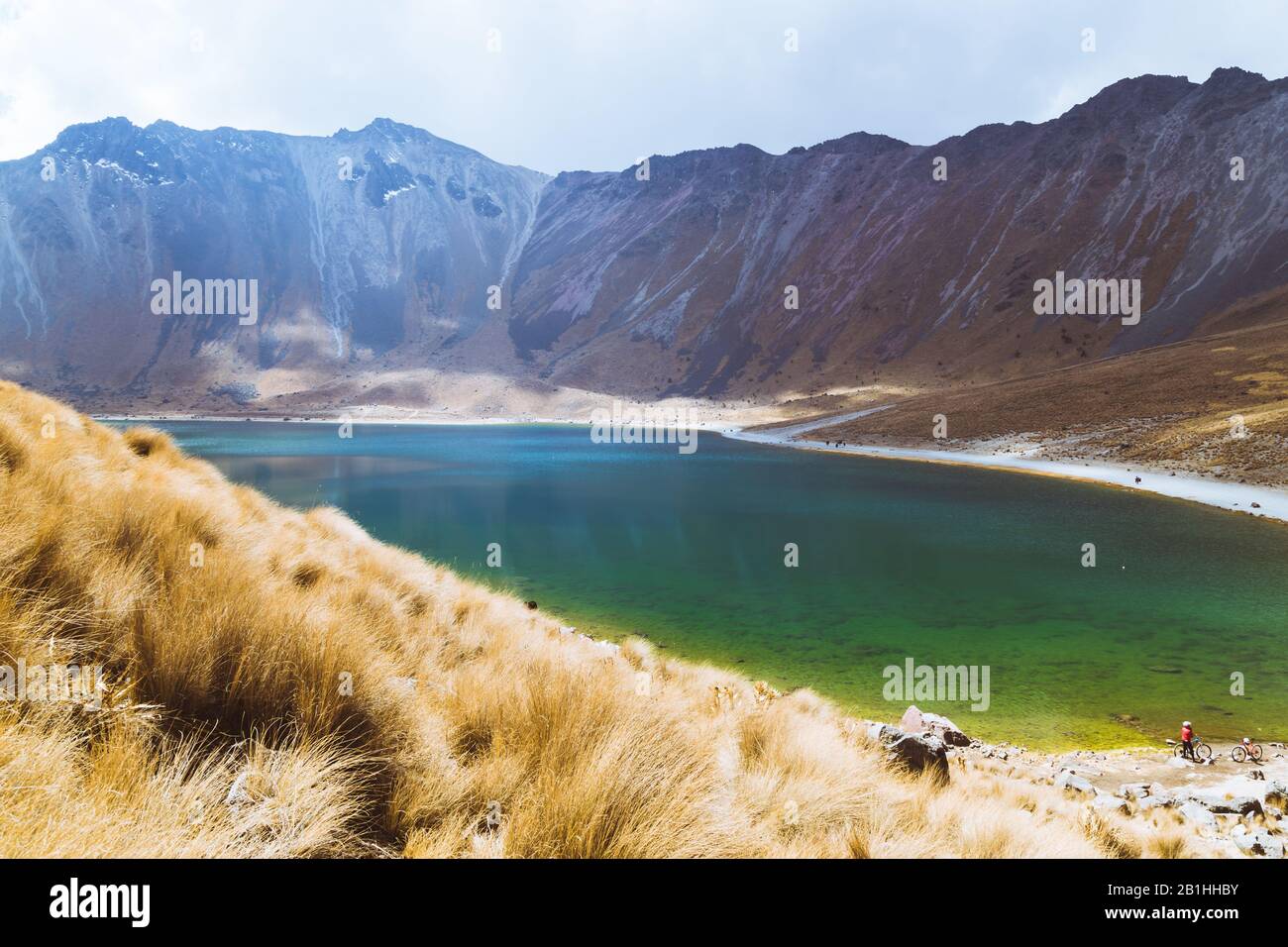 Un lago con aguas cristalinas, rodeado de montañas nevadas y un cielo azul con nubes Foto de stock
