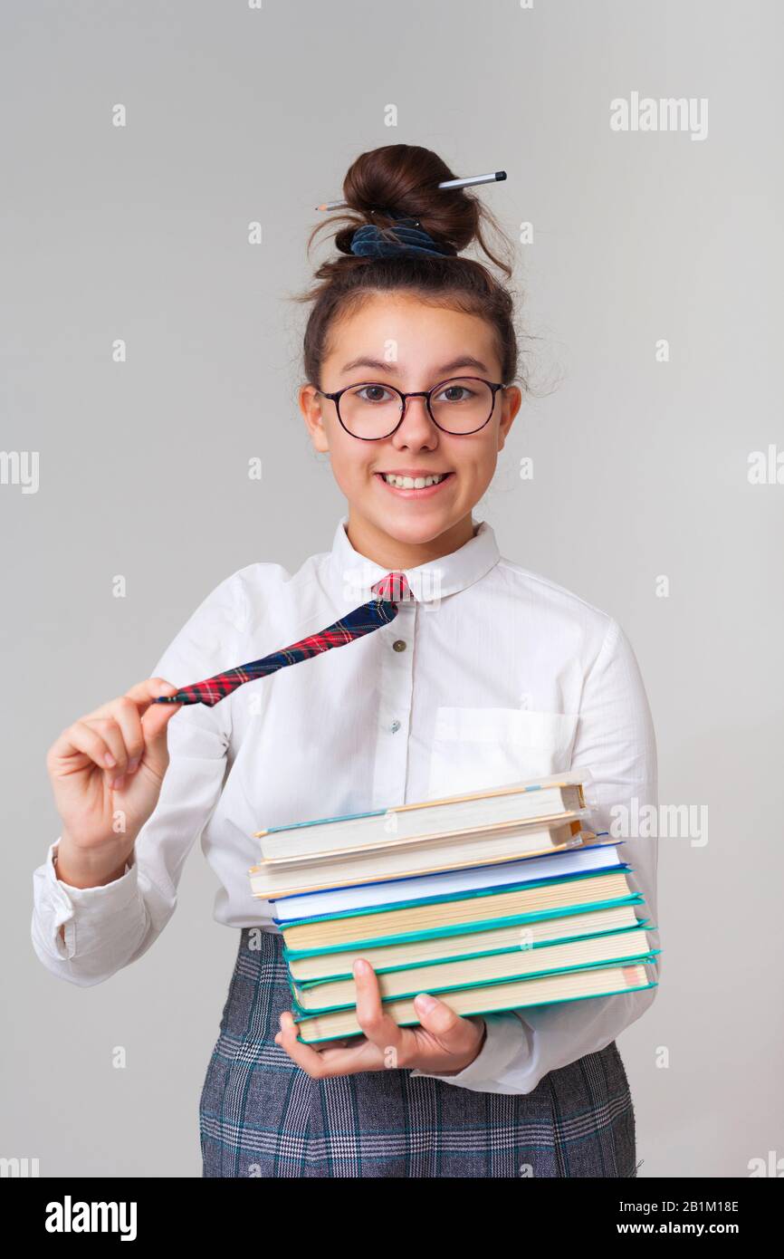 A una chica hermosa y feliz le encanta estudiar. Una colegiala con gafas y  corbata sostiene una pila de libros. Estudiar literatura. Club escolar  después de clase. Aprender un idioma extranjero Fotografía