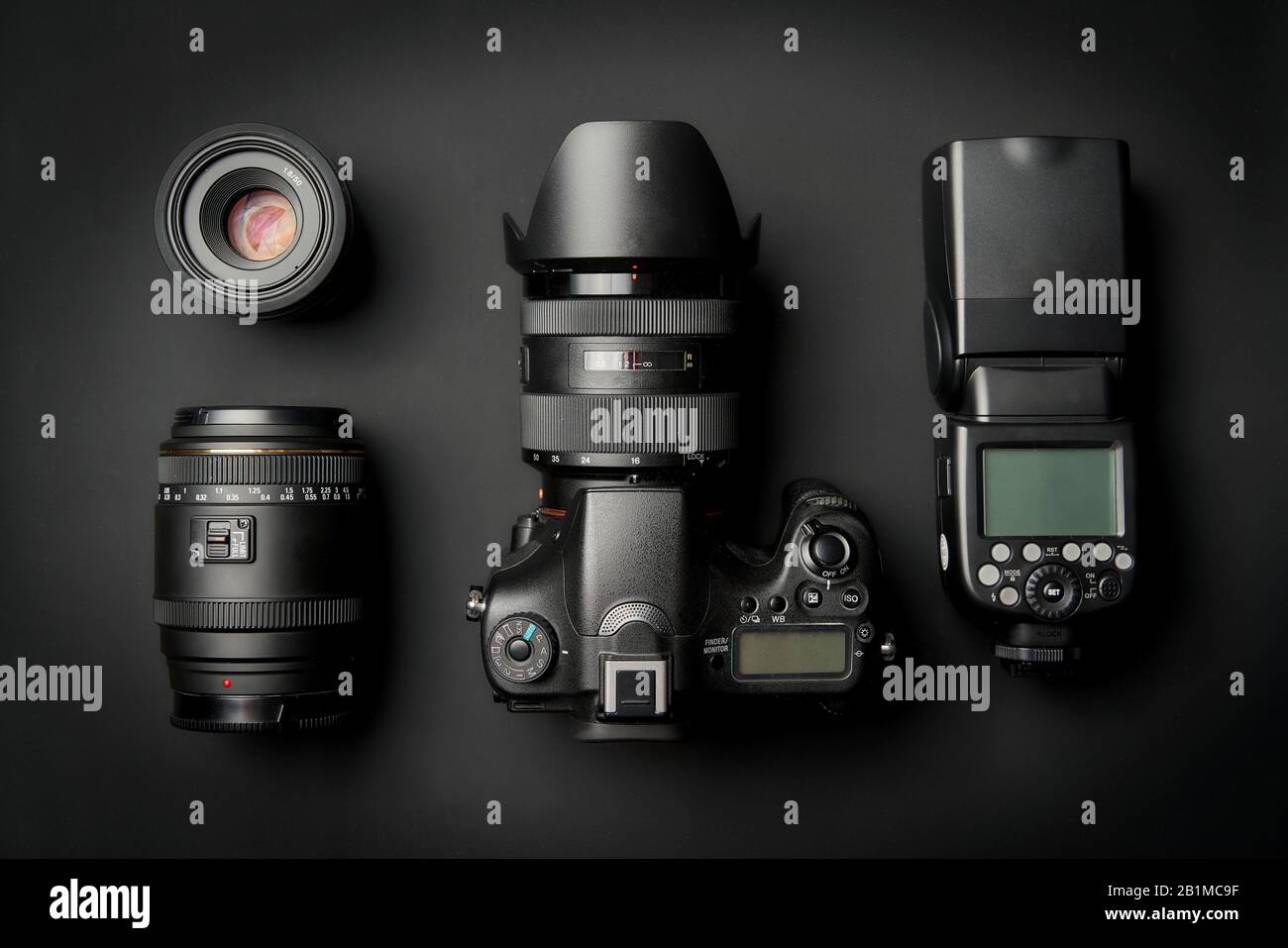 Vista superior del moderno equipo de cámaras digitales: DSLR con lente de zoom y capucha, lentes y linterna externa sobre superficie negra Foto de stock