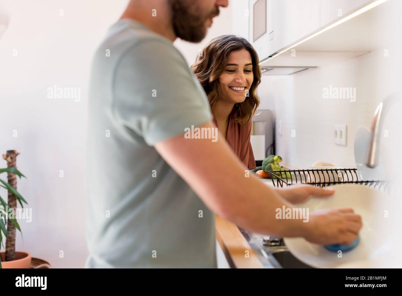 Pareja compartiendo tareas domésticas. Mujer feliz viendo a un hombre lavando platos. Foto de stock