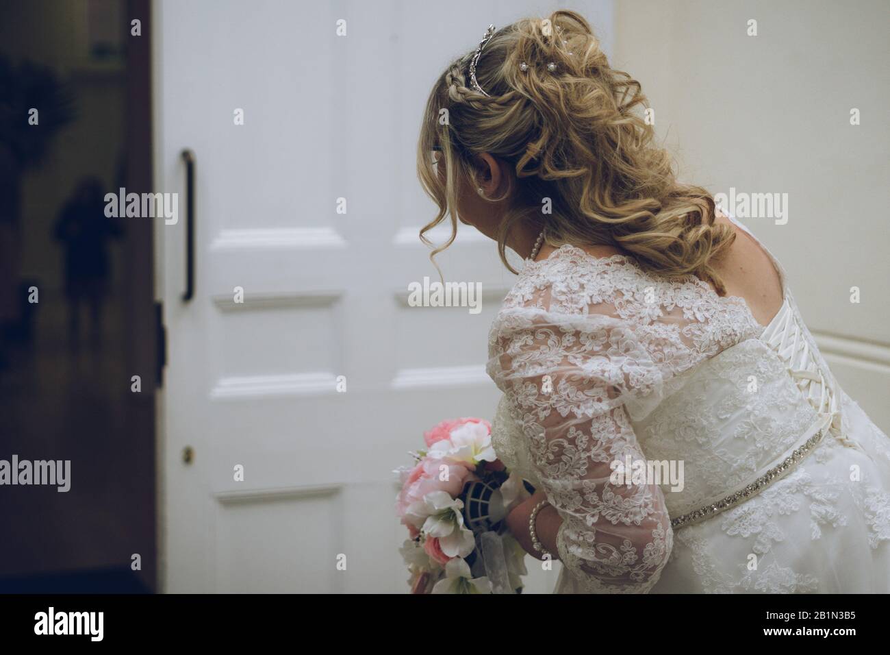Una novia nerviosa antes de su boda peeking a través de la puerta de la iglesia Foto de stock