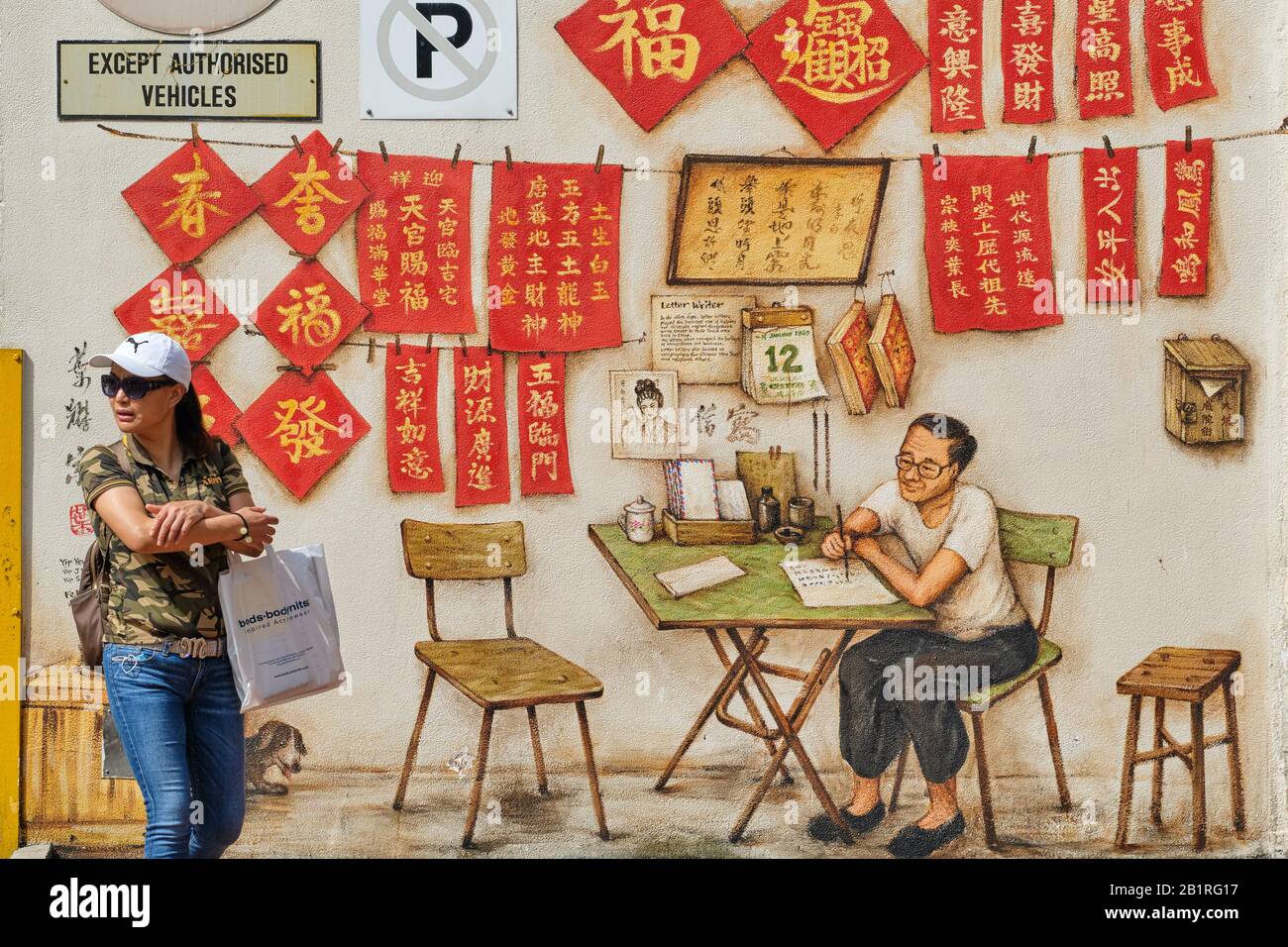 Una mujer pasa por una pintura mural en el Complejo Chinatown, Smith St., Chinatown, Singapur, que representa a un escritor de letras chino profesional y un caligrafía Foto de stock
