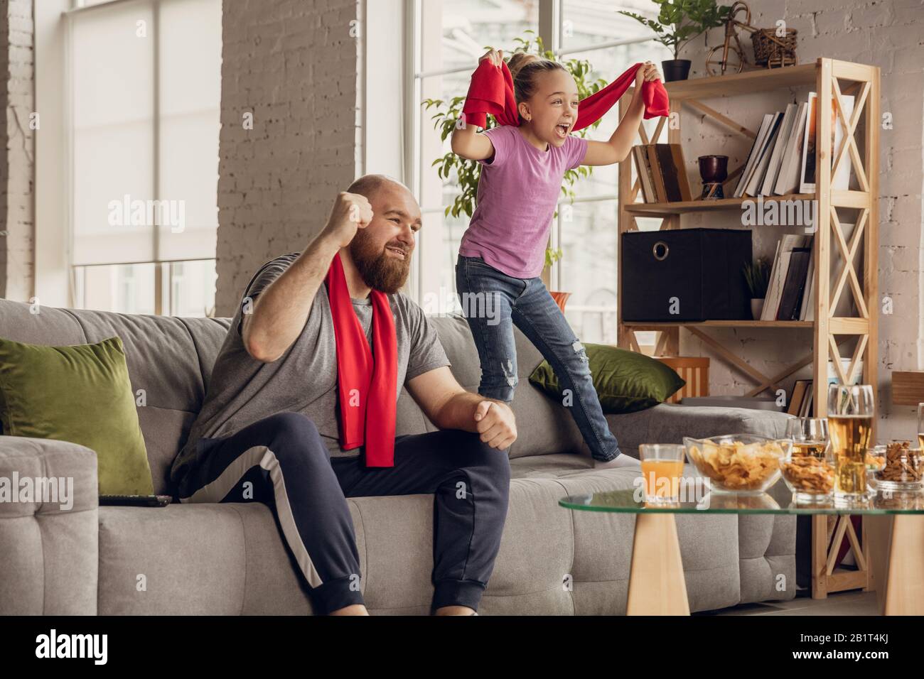 Emocionado, feliz hija y padre viendo fútbol, fútbol, baloncesto, tenis,  hockey partido en el sofá en casa. Fans animan emotivo a tu equipo nacional  favorito. Deporte, TV, campeonato Fotografía de stock -